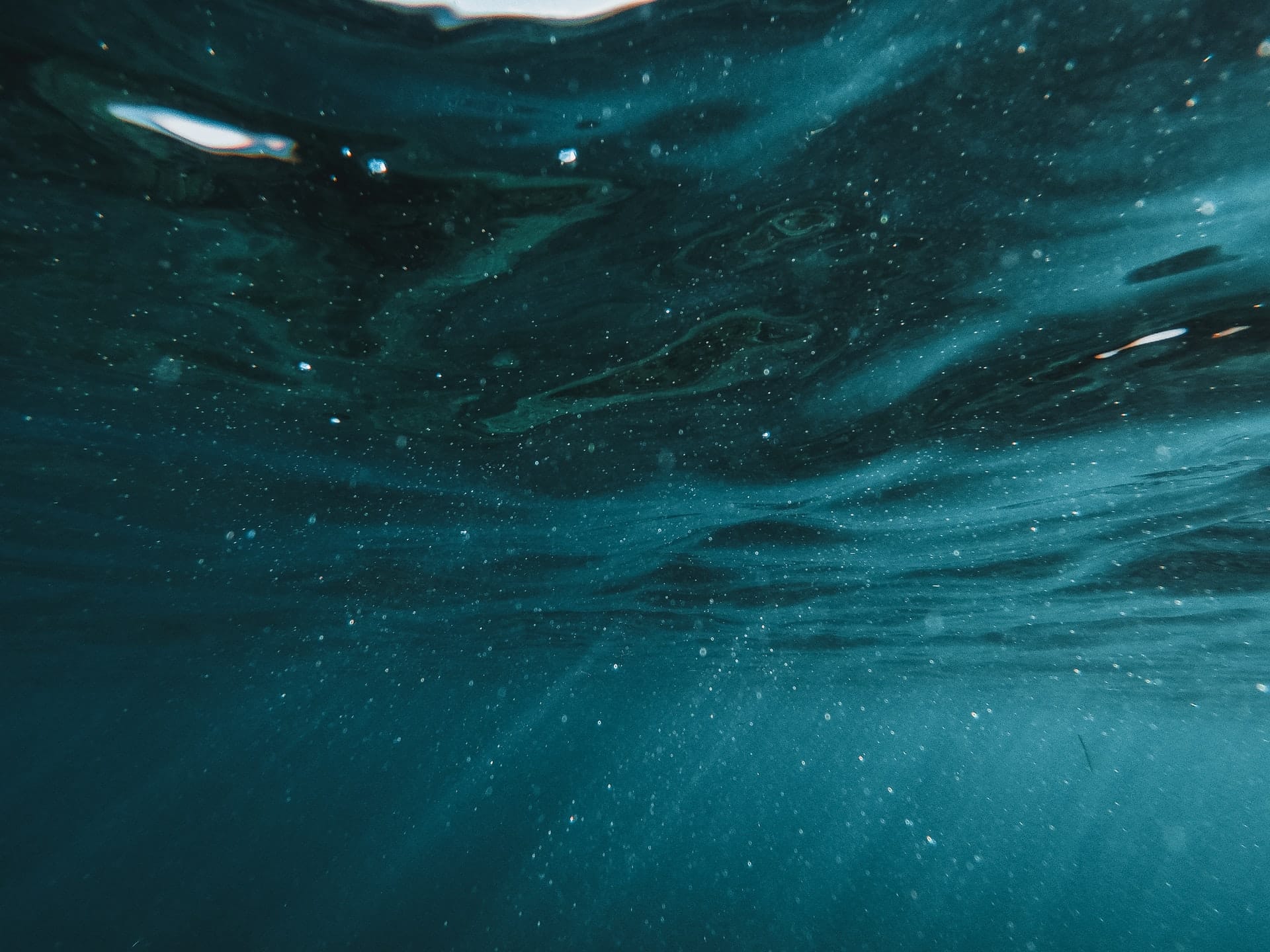 Underwater view of turquoise seawater with suspended particles and light rays from the surface.