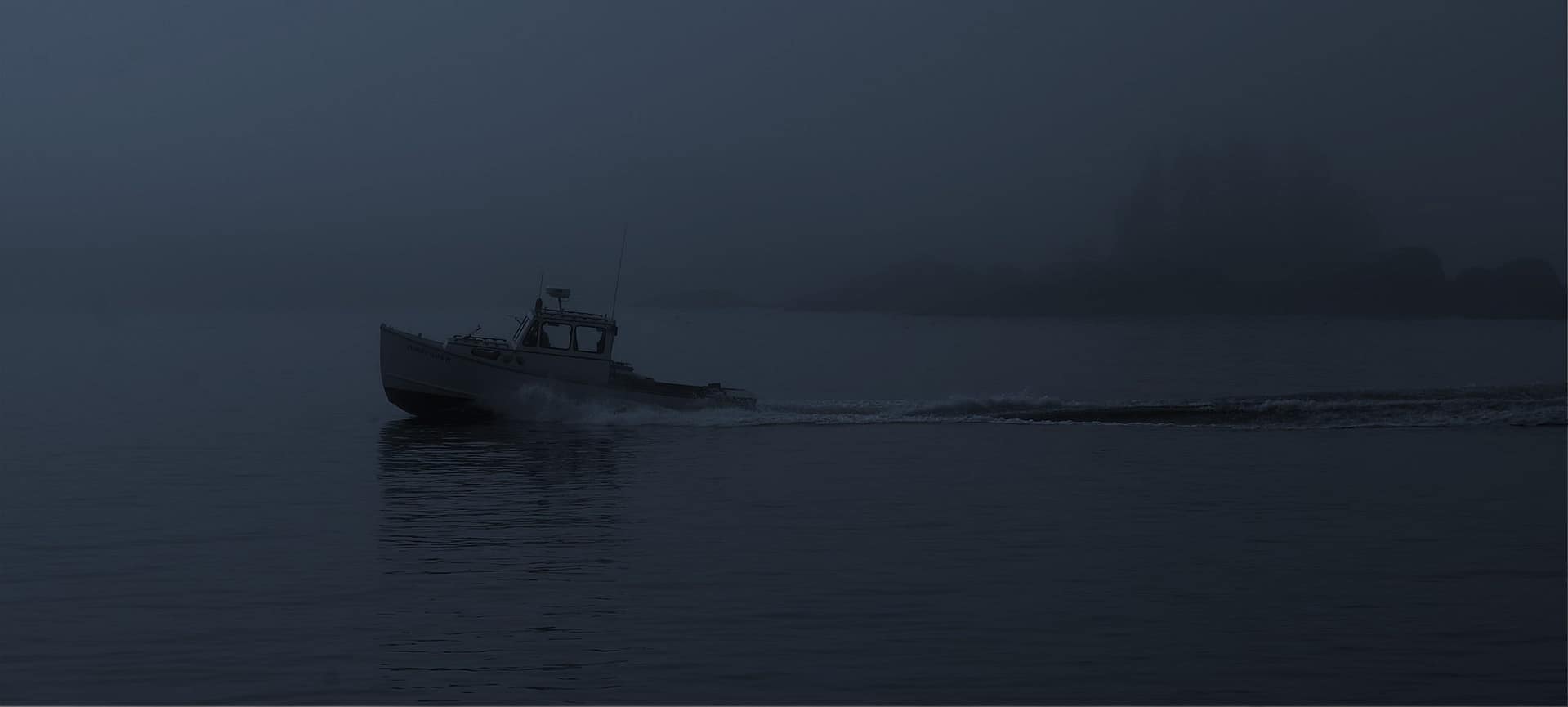 Small work boat moving across calm water in heavy coastal fog with distant shoreline barely visible.