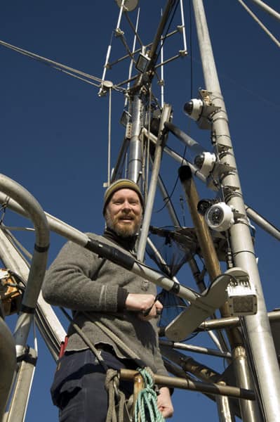 Fisheries technician standing on a fishing vessel mast surrounded by electronic monitoring cameras and antennas.